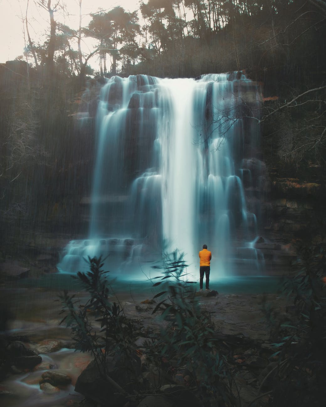 unrecognizable man standing near waterfall streaming through stones